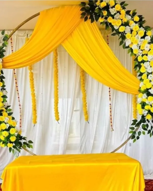 A beautiful Haldi ring backdrop with yellow and white flowers, perfect for an elegant ceremony. The setup includes a table covered in matching yellow fabric for placing ritual items.