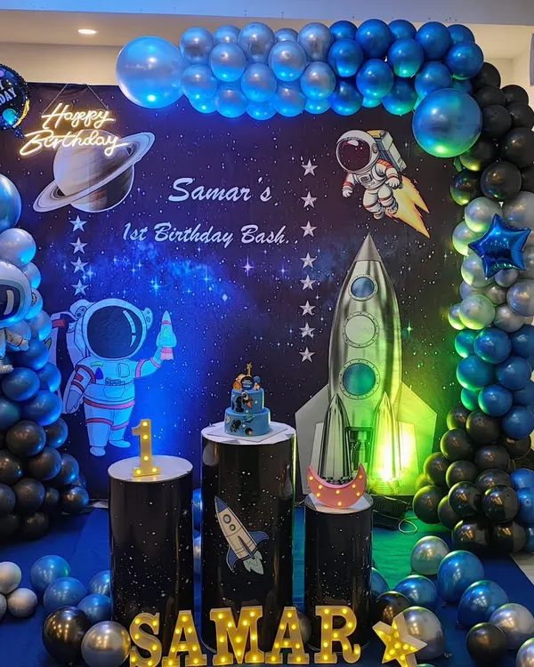 Here is another take on the popular astronaut theme for a first birthday. This setup features a large galaxy backdrop, character cutouts, and a blue, black, and silver balloon arrangement.