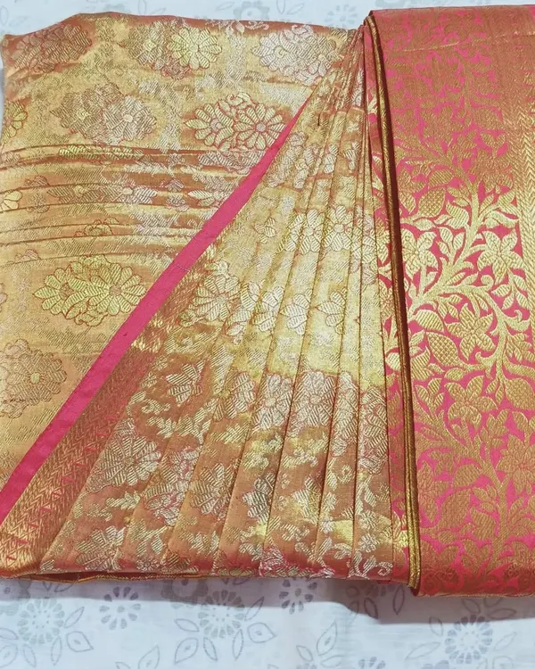A close-up of a pre-pleated and folded silk saree in gold and pink. The pleats are perfectly aligned and pressed, showcasing the neatness of the final folded product.
