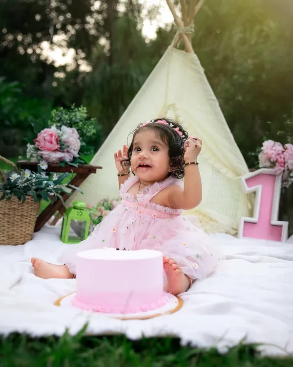 The best part of a cake smash is getting messy. This little princess is enjoying her first birthday cake in a beautiful garden setting, a perfect theme for an outdoor celebration.