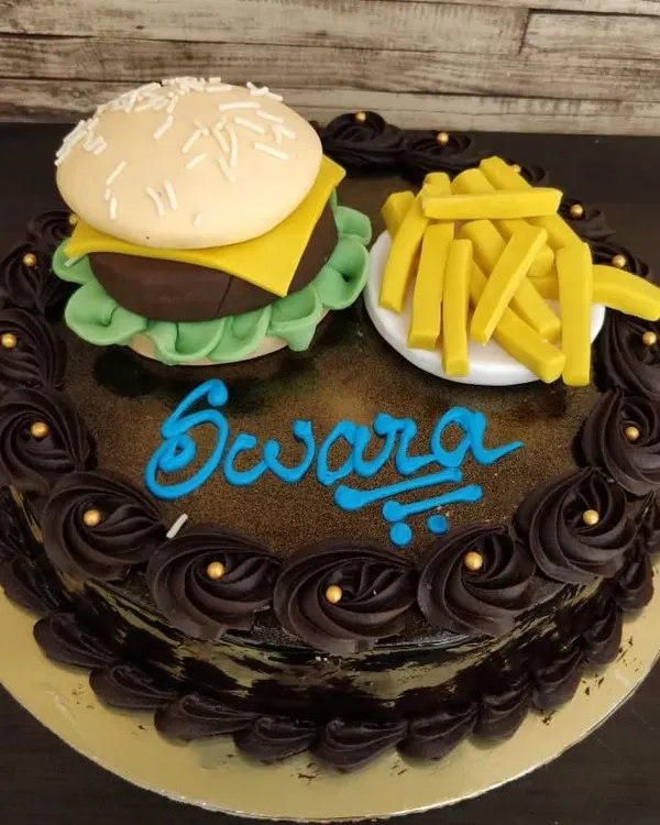 A cake that looks good enough to be a meal! This novelty cake features a meticulously sculpted fondant burger and a side of fries on top of a rich chocolate cake, perfect for a fast-food lover.