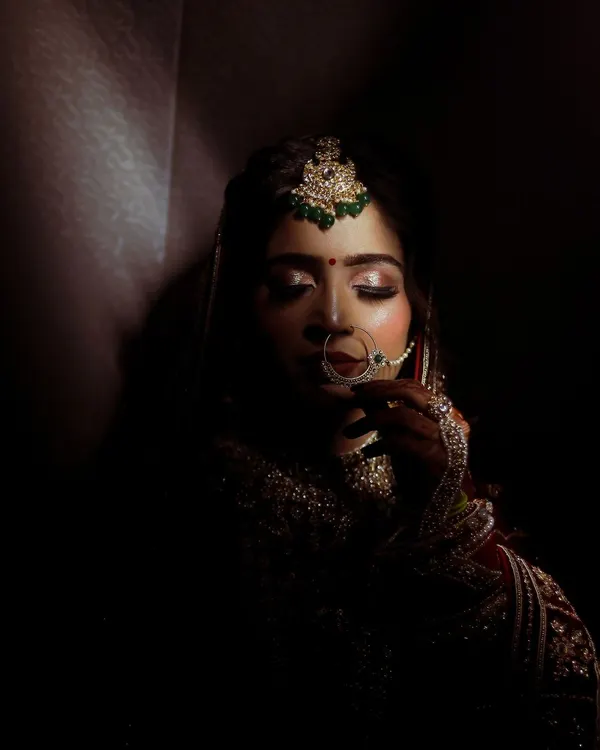 Using shadow and light to create a dramatic and soulful bridal portrait. This shot focuses on the bride's serene expression and the intricate details of her maang tikka and nath, creating a timeless, artistic image.
