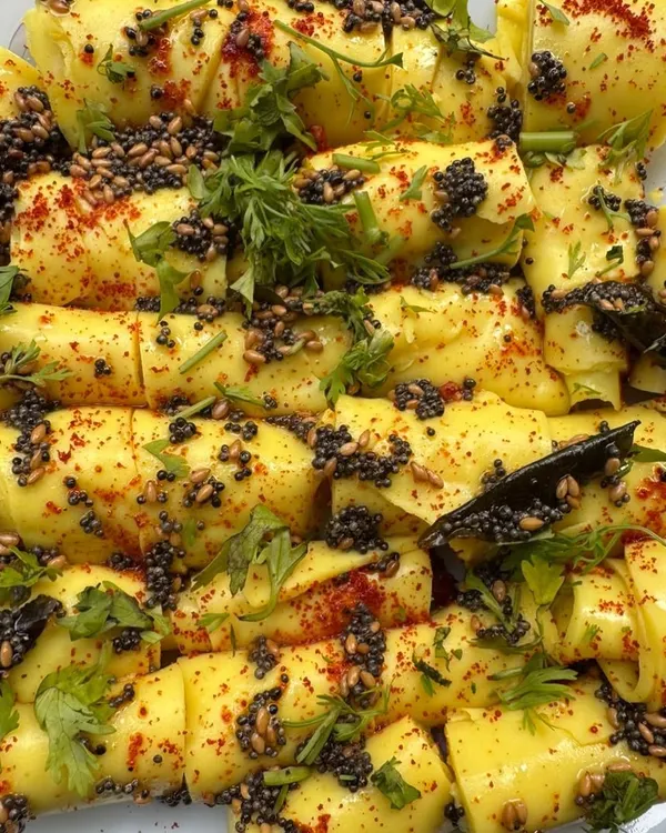 A platter of our delicate, paper-thin Khandvi rolls. These savory gram flour snacks are seasoned with mustard seeds, sesame seeds, and fresh cilantro, making them melt-in-your-mouth delicious.