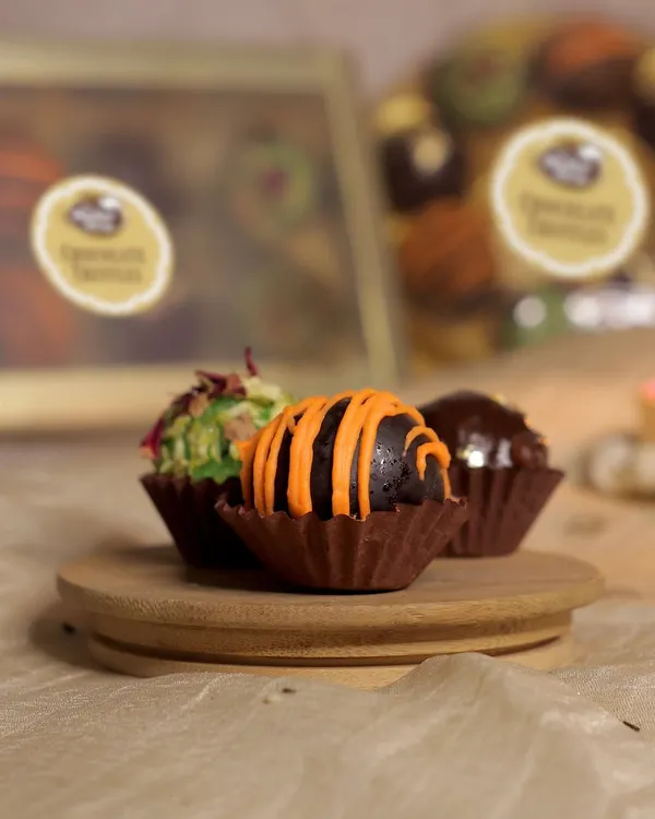A close-up of our assorted chocolate truffles. This shot highlights the vibrant orange-drizzled chocolate orange truffle, the delicate coconut rose truffle, and a rich dark chocolate hazelnut truffle.
