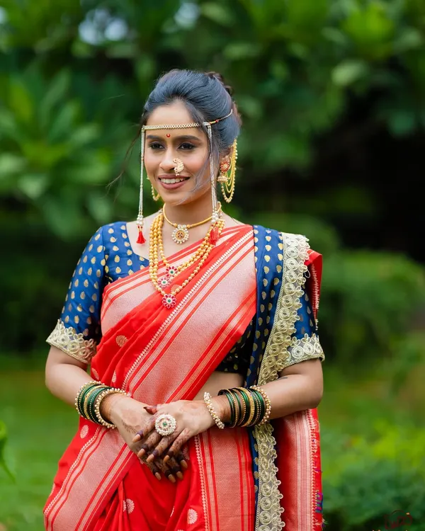 A classic Maharashtrian bridal look featuring a vibrant red Paithani saree. The makeup is kept minimal and radiant to highlight her natural features, complete with traditional jewelry like the mundavalya and nath.