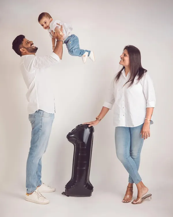A classic first birthday studio shot. The dad lifting his son in the air captures the pure joy of this milestone, with the number '1' balloon marking the day.