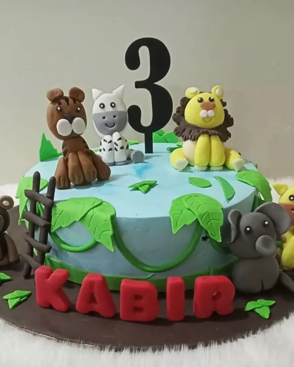 A wild jungle adventure for a third birthday. This cake is decorated with hand-molded fondant animals like a lion, elephant, and monkey, set around a jungle watering hole.