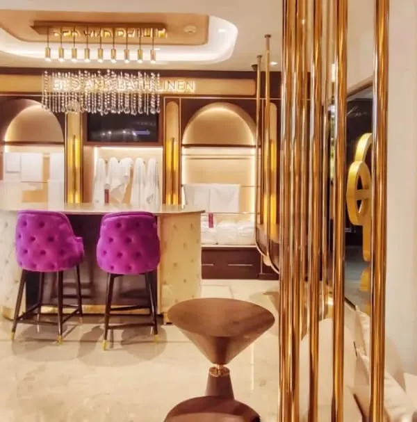 The main counter and seating area at the Sleeep Boutique, designed to feel both exclusive and welcoming. The combination of gold metal screens, a marble counter, and bold fuchsia chairs defines the space's playful opulence.