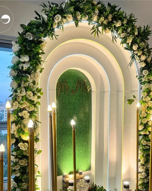 For an intimate home ceremony, we designed this modern and romantic backdrop. The layered arches, soft backlighting, and a lush floral garland of white roses created a dreamy focal point for the couple to exchange their promises.