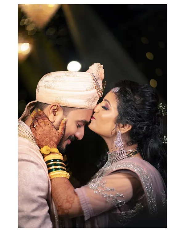 A quiet moment of affection. The groom's gentle kiss on the bride's forehead is a timeless expression of love that we love to capture. This candid wedding portrait highlights the couple's connection amidst the celebration.