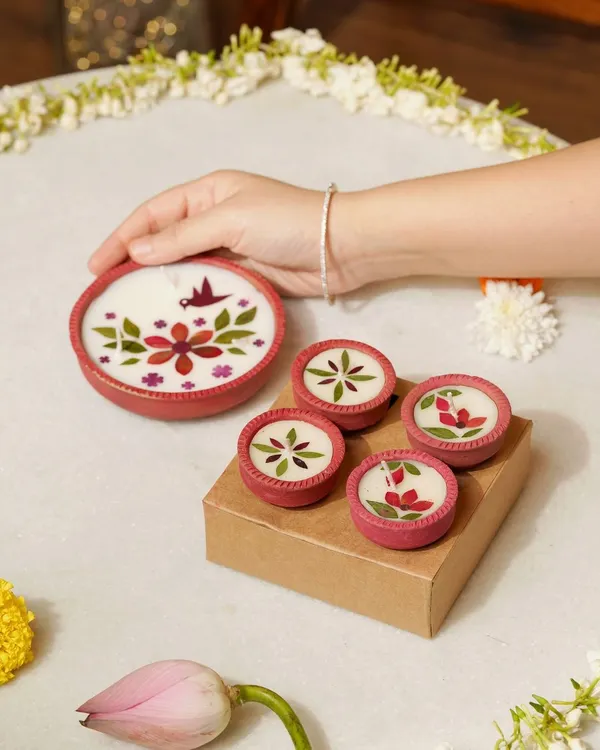 A hand gently arranges beautifully handcrafted diyas made with dried flowers. This shot highlights the artistic detail and traditional charm of the product, perfect for Diwali gifting and decor.