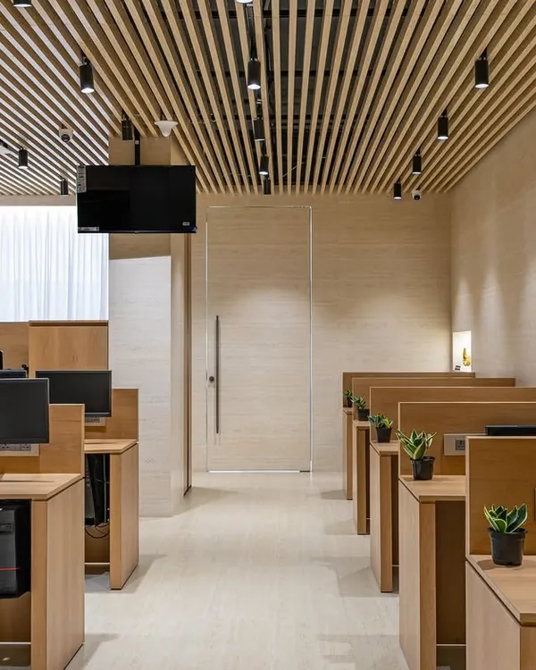A view of the main workstation hall in 'The Terra Office'. The design emphasizes a cohesive look with matching wooden desks and a continuous fluted wooden ceiling that adds architectural interest and warmth.