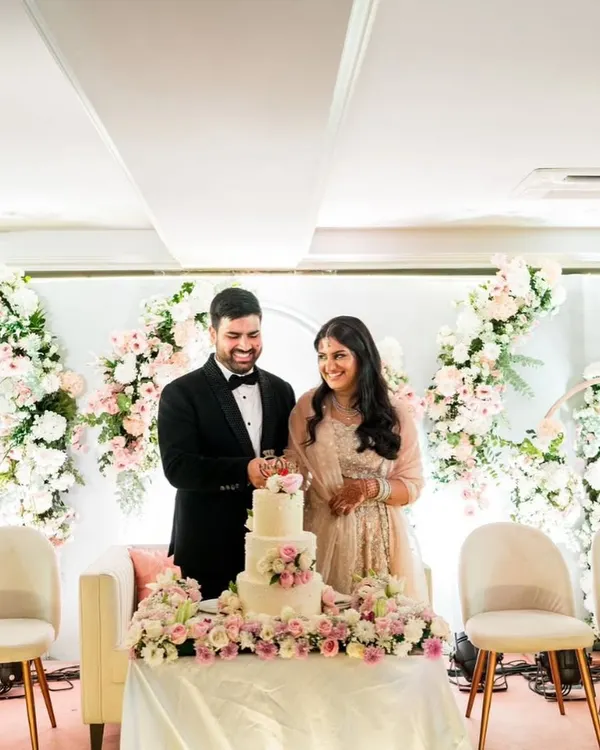 A beautiful moment of a couple cutting their three-tiered wedding cake. Set against a stunning floral backdrop, this cake featured layers of chocolate ganache, praline, and strawberry fresh cream.