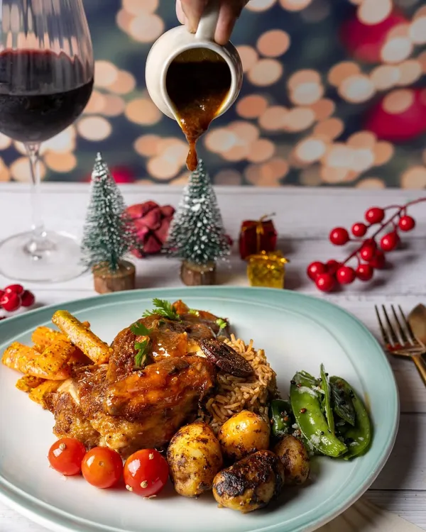 A festive plate of roasted lamb shank with a glass of red wine, set against a backdrop of twinkling Christmas lights.