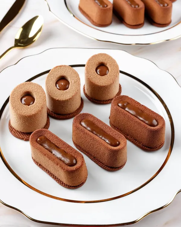 The clean lines and velvety texture of these chocolate entremets are highlighted with precise lighting for a high-end patisserie look.