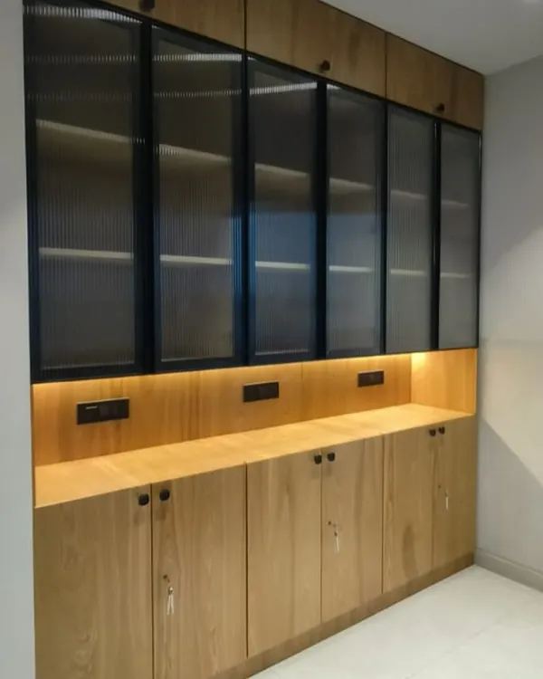 This custom storage unit was designed for a modern office, blending natural wood tones with fluted glass doors. The integrated backlighting provides a warm ambiance while showcasing the items on display.