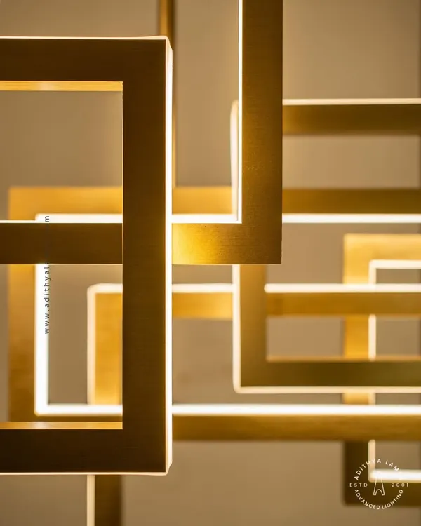 A multi-layered chandelier composed of intersecting rectangular frames with a brushed gold finish. The integrated LEDs cast a warm, ambient light, creating a dynamic and architectural statement piece for modern interiors.