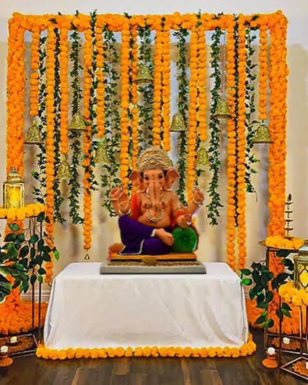 A traditional Ganpati decoration using marigold flower garlands and brass bells to create a beautiful and auspicious backdrop for the idol.