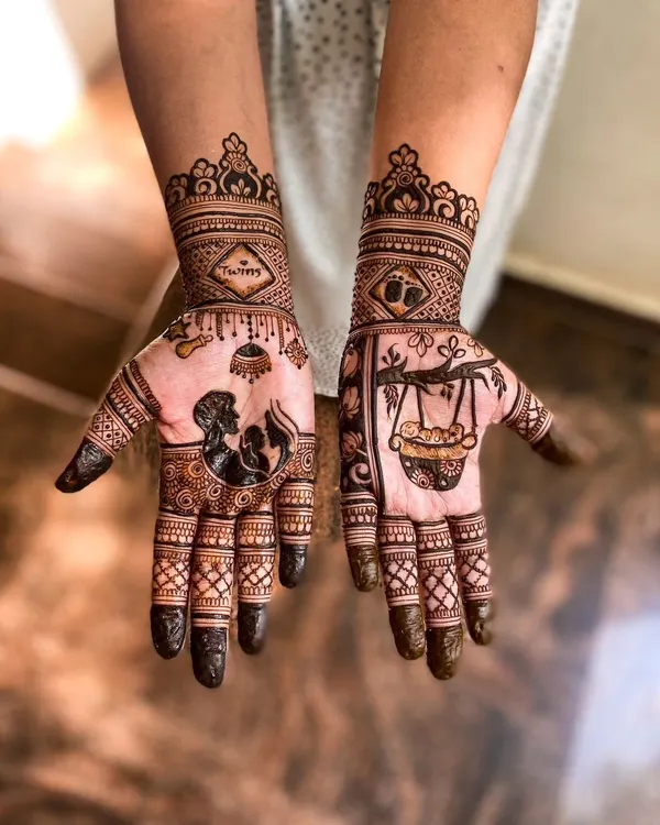 A very special baby shower mehendi for a mother expecting twins. One hand features a silhouette of parents with a baby, and the word 'Twins' is written on the wrist. The other hand has a drawing of a baby in a traditional cradle.
