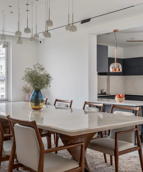 We specialize in creating cohesive, open-plan living areas. This view shows how the elegant dining space, with its onyx tabletop and statement lighting, flows seamlessly into a modern, minimalist kitchen. This approach enhances natural light and creates a perfect environment for family life and entertaining.