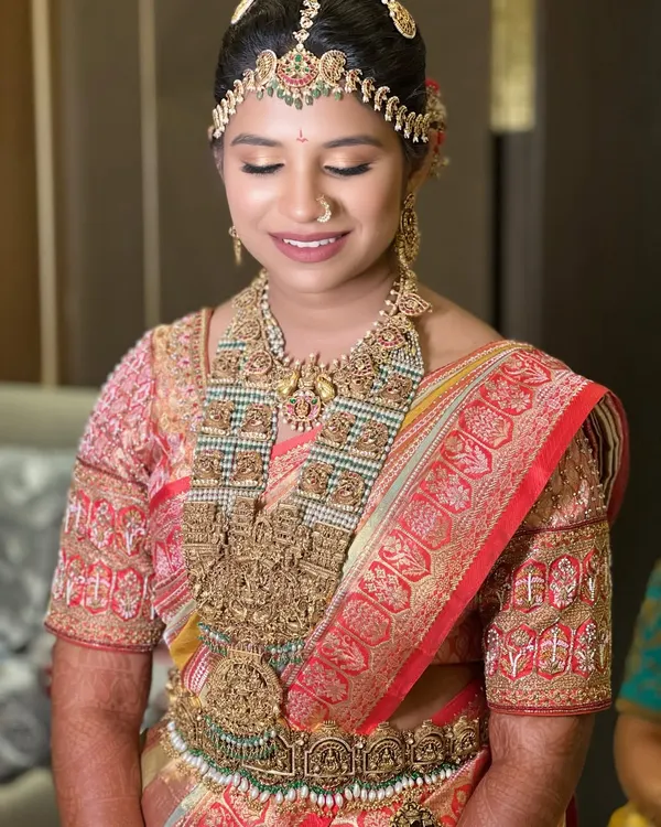Glowing in her wedding beauty, this enchanting bride radiates sophistication and bliss. Her look features a red and gold saree with heavy temple jewellery, and a soft, radiant makeup finish.