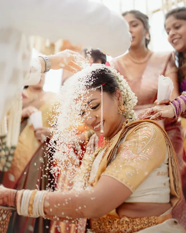 A beautiful moment from a South Indian wedding ceremony, where the bride is showered with sanctified rice. The bride's joyful expression is a perfect picture of tradition and happiness.