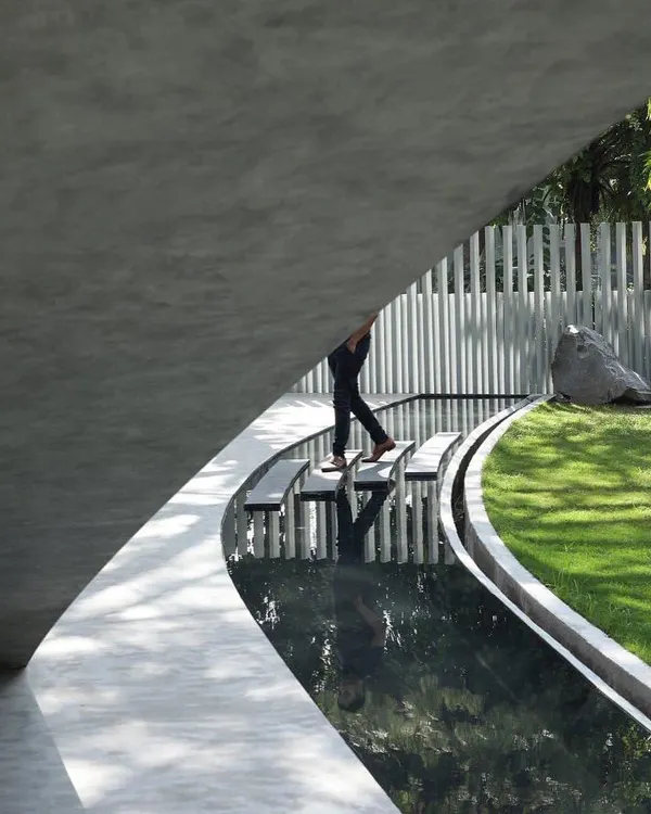 A unique perspective from beneath the curved roof of Villa KD 45, showing the stepping stones over a tranquil water body that guides you along the building's edge.