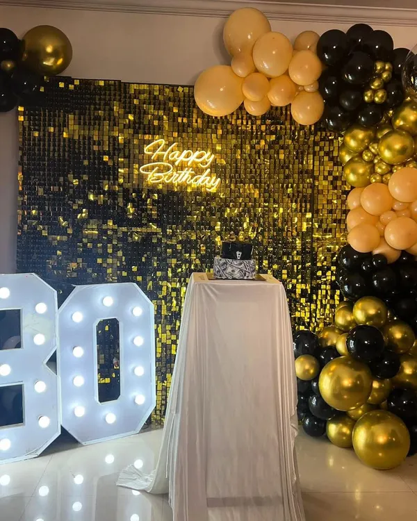 A classic and glamorous 30th birthday celebration. This setup features a gold sequin wall, a black and gold balloon arch, a "Happy Birthday" neon sign, and large light-up numbers for the big 3-0.