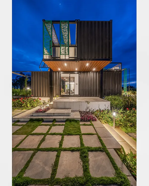 A striking twilight view of the QBINN TUSKER container home, where modern architecture meets the natural world. The strategic lighting highlights the structure's bold lines and the beautiful geometry of the landscaped walkway, creating an inviting glow against the deep blue evening sky.