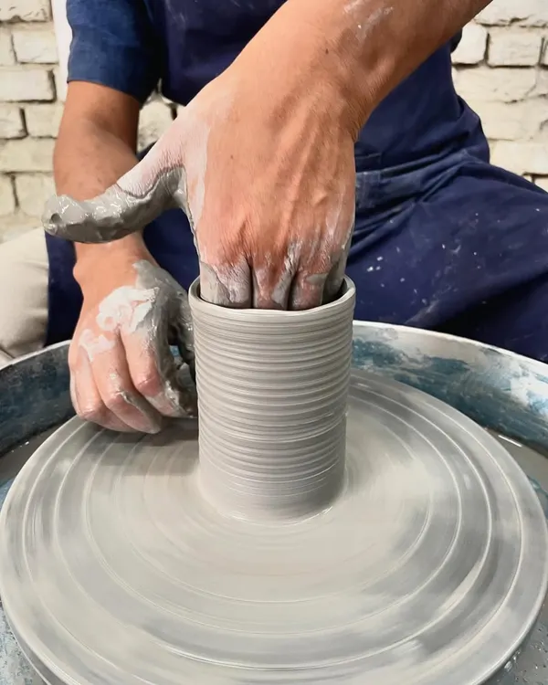 A close-up of my hands shaping the inside of a cylinder on the wheel. This is where you feel the clay and guide it upwards, creating the basic form.