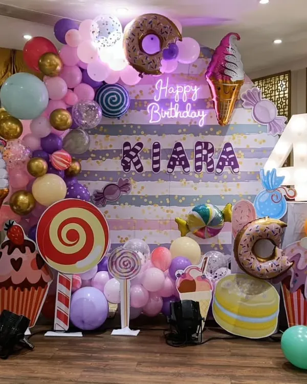 A full-stage Candyland theme for Kiara's 4th birthday, featuring a custom backdrop, large candy props, and a vibrant balloon arch. This setup creates a sweet wonderland for kids.