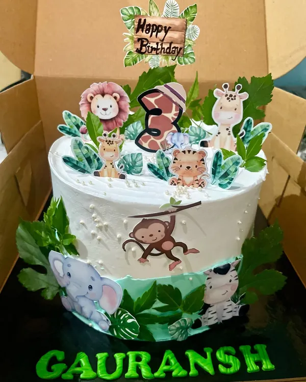 A wild adventure awaits with this jungle safari themed cake for a 3rd birthday. It's decorated with cute, edible prints of a lion, giraffe, and monkey, complete with lush green leaves to create a fun and festive centerpiece for a kid's party.