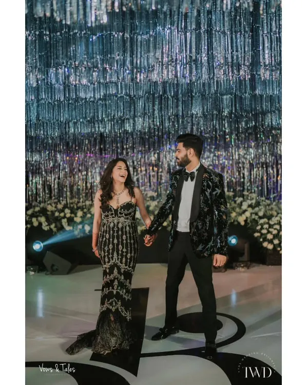 A glamorous couple ready for their cocktail night. Standing beneath a ceiling of shimmering silver tassels, their elegant attire and loving gaze set the tone for an evening of sophisticated celebration and dancing.