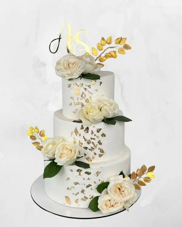 A classic white and gold three-tier wedding cake. The clean lines, delicate gold leaf, and fresh white roses create a look of timeless elegance for your big day.
