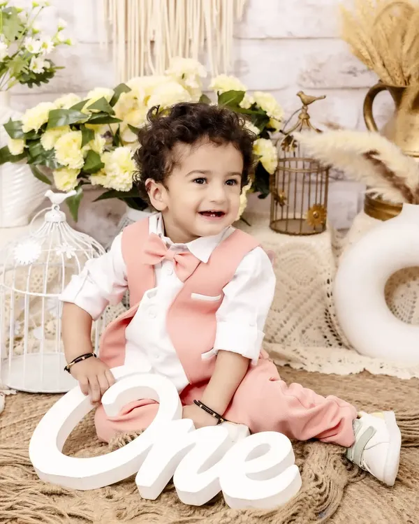 A picture-perfect moment for his first birthday celebration. Dressed in a charming pink vest and bow tie, this little one's happy smile is the centerpiece of this classic and elegant studio setup.