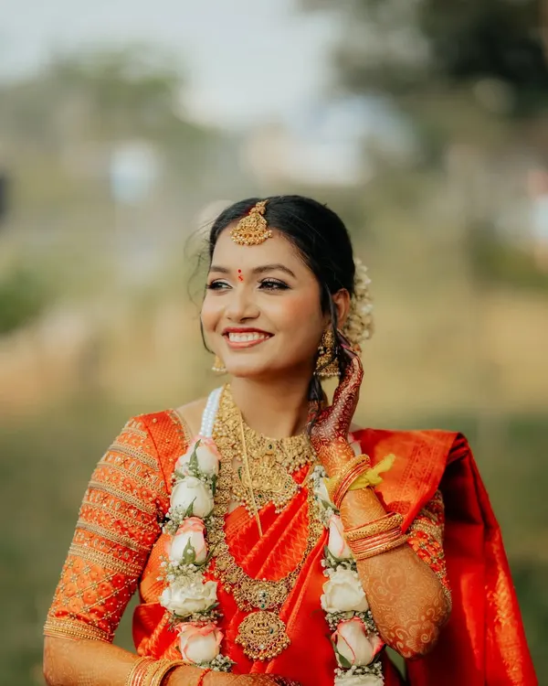 A radiant South Indian bride in her bright orange Kanjeevaram saree, adorned with temple jewelry and a floral garland.