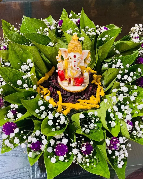 An auspicious tray arrangement perfect for starting any ceremony. A small Ganesha idol sits at the center of neatly arranged betel leaves, accented with baby's breath and purple flowers for a fresh and traditional look.