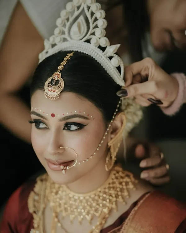 The final touches on my beautiful Bengali bride, Archita. Placing the 'topor' is such a significant moment. Her makeup features the classic winged liner and red bindi, essential elements of the tradition.
