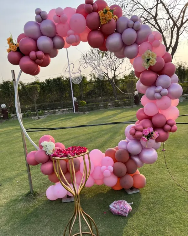 An elegant balloon ring setup for an outdoor garden party. This arch uses a sophisticated palette of pinks and reds, perfect for a daytime or sunset celebration.