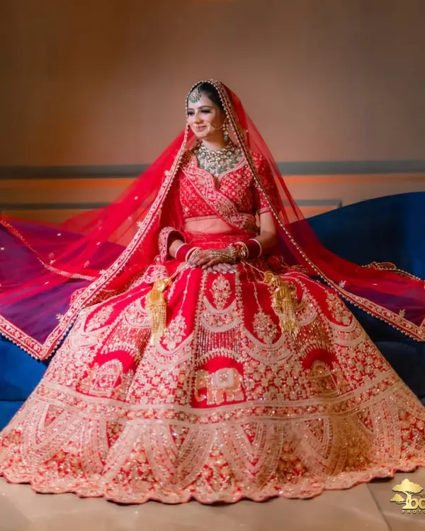 A breathtaking full-length portrait of the bride on a sofa, showcasing her magnificent red lehenga in all its glory. A truly regal bridal shot.