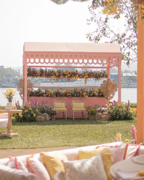A 'Riverside Brunch' in Goa with a charming pink stall set against the water. The design uses a soft pastel palette and lush florals for a relaxed, garden-party feel.