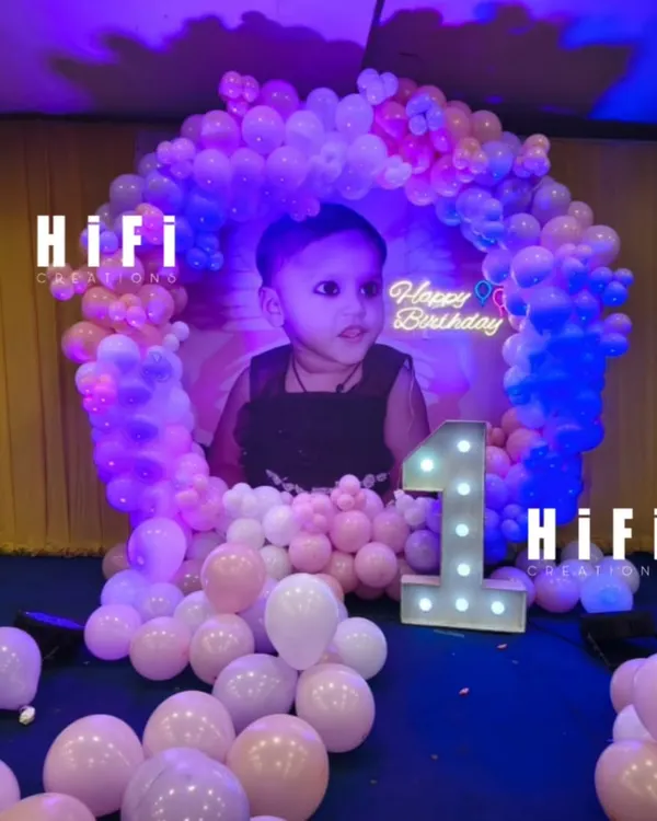 A sweet and simple first birthday setup right in the living room. We used a personalized photo backdrop, a pastel balloon arch, and a light-up number to create a special corner for the celebration.