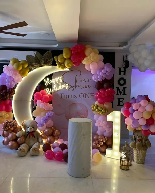A dreamy "Twinkle Twinkle Little Star" theme for a first birthday, featuring a crescent moon prop with a neon sign and a soft-colored balloon garland.