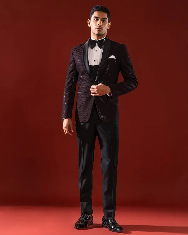 This three-piece tuxedo in a deep burgundy features a subtle, shimmering pattern on the jacket, paired with a classic waistcoat and bow tie. It is an ensemble designed for the gentleman attending a black-tie gala or a formal wedding reception.