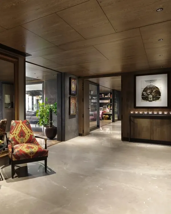 The entrance lobby of the Caitriona apartment in Gurugram, transformed with Sukupira wood veneer, Burberry Beige stone flooring, and olive grey walls. A pair of 'Arizona Armchairs' upholstered in a hand-woven durrie creates a welcoming vignette.