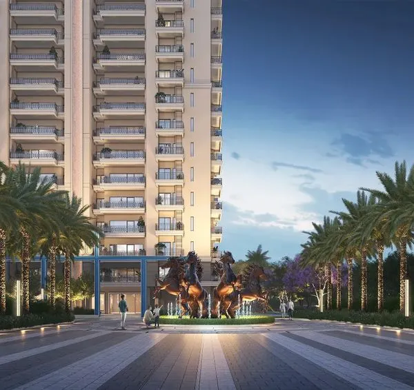 A statement entrance for a housing community in Greater Noida, featuring a grand water fountain with majestic horse sculptures. The wide road, flanked by an avenue of palm trees, creates an unforgettable and grand sense of arrival.
