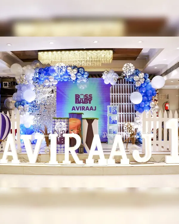 A complete stage setup for a "Boss Baby" first birthday, featuring a large LED screen backdrop, custom marquee letters, and a charming white picket fence.