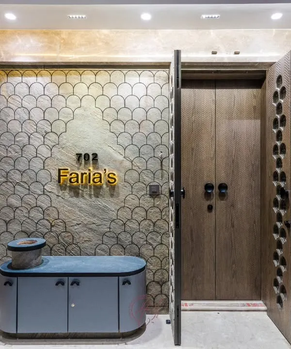 This stunning home entrance features a custom-designed main door with a unique perforated pattern, set against a wall with an intricate fish-scale texture. The wooden inner door adds a layer of warmth and security.