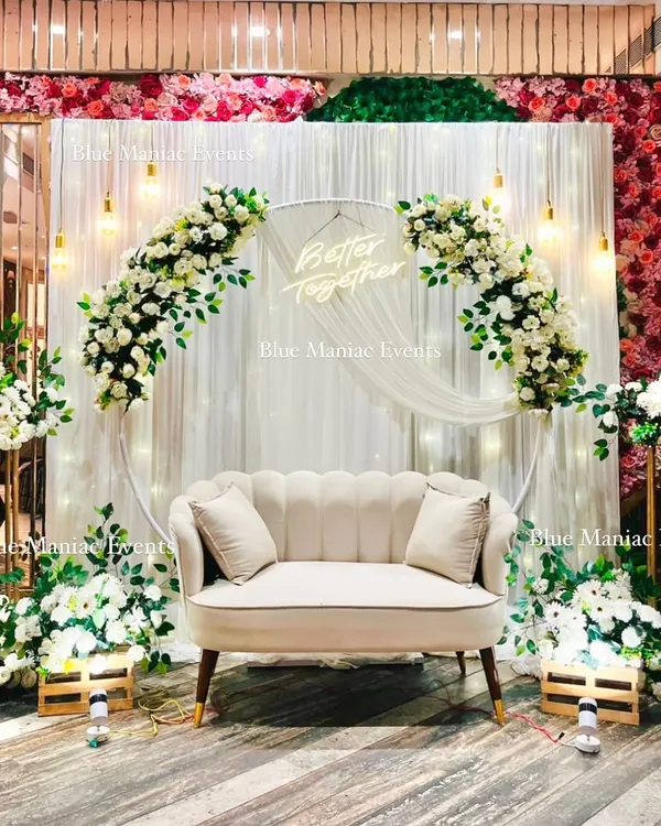 A full view of this beautiful white-themed Roka setup. The design includes a large floral ring, a 'Better Together' neon sign, and additional floral arrangements on stands, creating a complete and immersive photo corner in the venue.