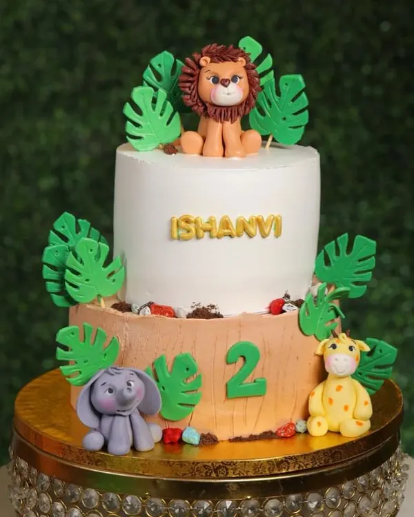 Welcome to the jungle! This two-tier cake is a wild adventure, featuring hand-sculpted fondant animals like a lion, elephant, and giraffe surrounded by lush jungle leaves.